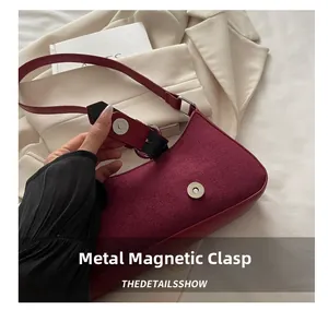 Detail view of the magnetic metal snap closure on a burgundy suede shoulder bag for women