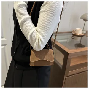 Detailed view of the wavy flap design on a brown suede mini crossbody bag worn by a model