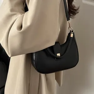 Minimalist black crescent hobo bag with gold hardware worn over a beige trench coat