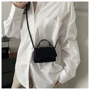 Close-up of small black suede crossbody bag styled on a white shirt in a minimalist setting