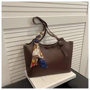 Close-up of dark brown leather tote bag with silk scarf detail and adjustable strap