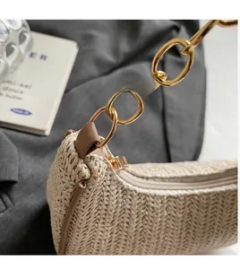 Detail of golden oval chain strap on beige woven straw crescent shoulder bag with leather edge
