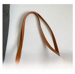 Detail view of reinforced brown leather handles and premium stitching on a tote bag