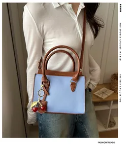 Détail du sac en cuir bleu clair avec coutures marron et breloque cerise élégante