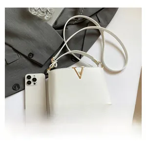 Detail van de witte handtas met gouden V-logo naast een smartphone voor de maatreferentie