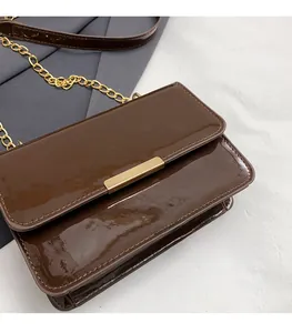 Detail of glossy brown patent leather crossbody bag with elegant gold metal buckle and chain