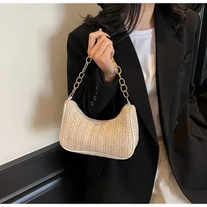Detailed macro of woven straw crescent bag featuring elegant gold chain strap and leather trim