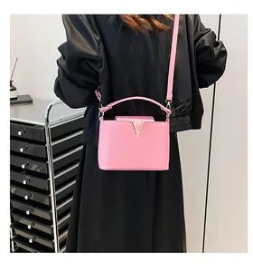 Detail van roze handtas met gouden V-vormige hardware en verstelbare schouderriem