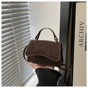 Detail of a dark brown suede crossbody bag with wave flap design and top handle