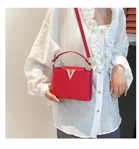 Gros plan d'un sac à main en cuir rouge avec boucle dorée en V et bandoulière