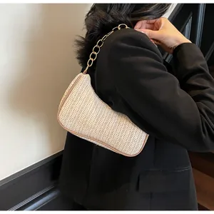 Detail of beige woven crescent bag with thick gold chain and brown piping on a model