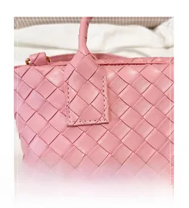 Detail of pink woven leather texture and stitched handle attachment on shoulder bag