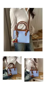 Detail of blue pebble grain handbag with brown leather trim and red cherry charm accessory