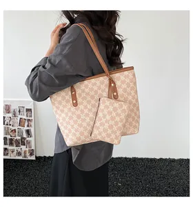 Detail of a large beige tote bag with M-pattern and brown leather handles on a model
