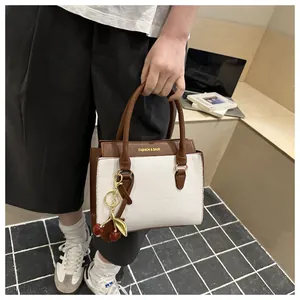 Détail d'un sac à main bicolore en cuir grainé avec un pendentif cerise décoratif