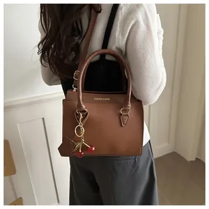Sac à main marron grainé avec lettrage doré et un charmant pendentif cerise