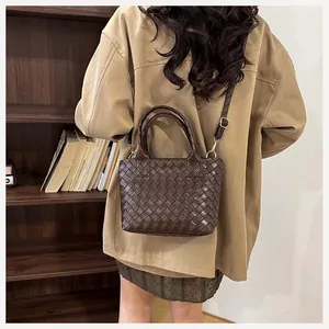 Detail of dark brown woven leather bag with dual handles and golden hardware accents