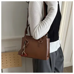 Detail of caramel brown handbag with cherry charm and gold hardware on white background