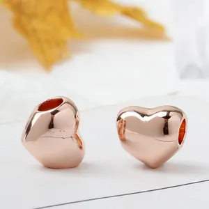Polished rose gold heart charms for DIY bracelets shown with autumn leaf background