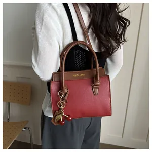 Détail du sac à main bordeaux en cuir grainé avec pendentif cerise sur fond minimaliste