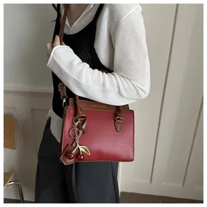 Detail view of burgundy crossbody bag with brown trim and cherry pendant accessory