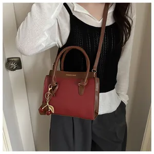 Détail du petit sac bandoulière rouge avec breloque cerise et anses marron sur le mannequin