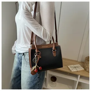 Détail d'un sac à main bicolore noir et marron avec charm cerise et finitions dorées