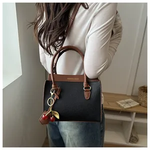 Détail du sac à bandoulière bicolore avec pendentif cerise et texture en cuir grainé