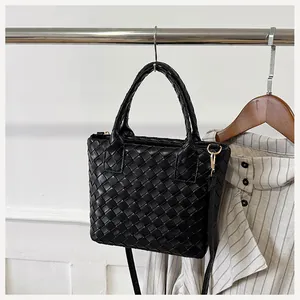 Close-up of black woven leather texture on a Boston bag with gold lobster clasp detail