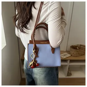Détail du sac cabas bicolore en cuir avec breloque cerise et texture grainée élégante