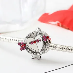 Macro view of Cupid's arrow bead and heart charm on silver snake chain bracelet