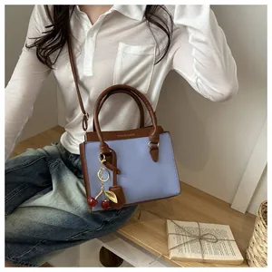 Close-up of a lilac textured leather crossbody bag featuring a cute cherry pendant charm