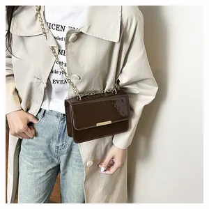 Detail showing high-gloss patent leather texture and gold metal bar on deep brown bag