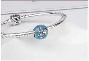 Close-up of silver snake chain bracelet featuring a blue enamel paw print charm detail
