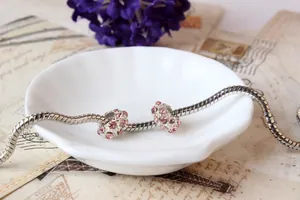 Silbernes Schlangenarmband mit rosa Strassperlen auf einer weißen Keramikplatte
