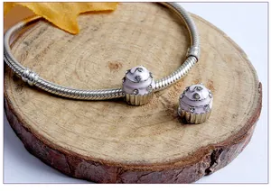 Macro shot of silver snake chain bracelet with pink enamel cupcake pendants on wood