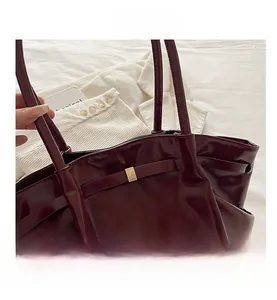 Detail view of the deep red glossy patent leather texture and gold buckle on the tote bag