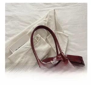 Close-up of wine red glossy leather tote bag featuring slim handles and metal buckle detail
