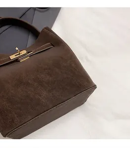 Details einer dunkelbraunen Wildleder-Umhängetasche mit goldenem Metalldrehverschluss