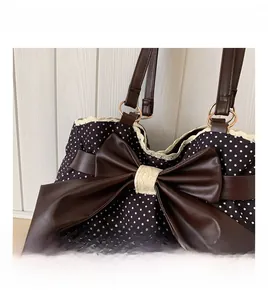 Close-up of a large leather bow and lace trim on a black polka dot tote bag surface