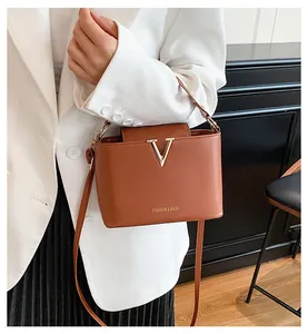 Close-up of caramel leather bucket bag featuring gold V-buckle on white blazer outfit