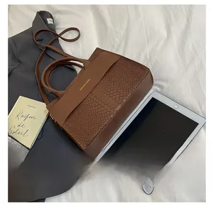 Brown tote bag with crocodile texture next to a tablet showing its large capacity