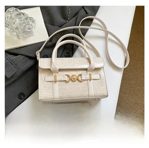 Close-up of ivory crocodile-embossed leather bag with gold heart clasp and smartphone comparison