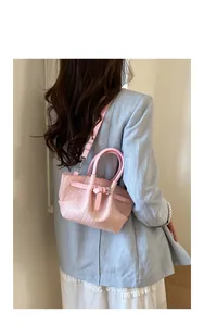 Model wearing a pink woven bucket bag with elegant circular handle and slim shoulder strap