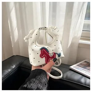 Detail of a mini white leather bag with heart prints and a red knitted horse patch