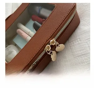 Détail des doubles fermetures éclair dorées et fenêtre transparente sur trousse brune