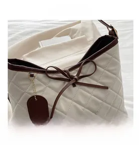 Detail view of white quilted tote bag with brown leather trim and bow decoration