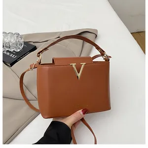 Detail of a brown leather bucket bag featuring a golden V-buckle and elegant handle