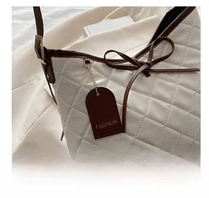 Detail of white quilted tote with brown bow and golden fashion tag on creased fabric
