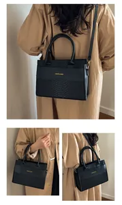 Detail view of a black tote bag with croc-texture panels and gold metal hardware